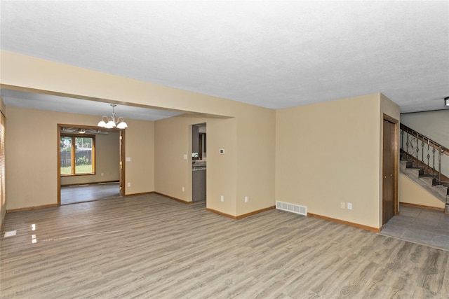 unfurnished living room with a textured ceiling, a notable chandelier, and light hardwood / wood-style floors