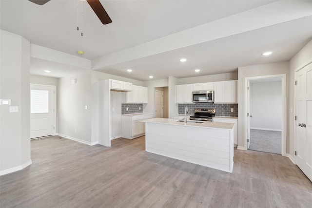 kitchen featuring stainless steel appliances, an island with sink, white cabinets, and light hardwood / wood-style flooring