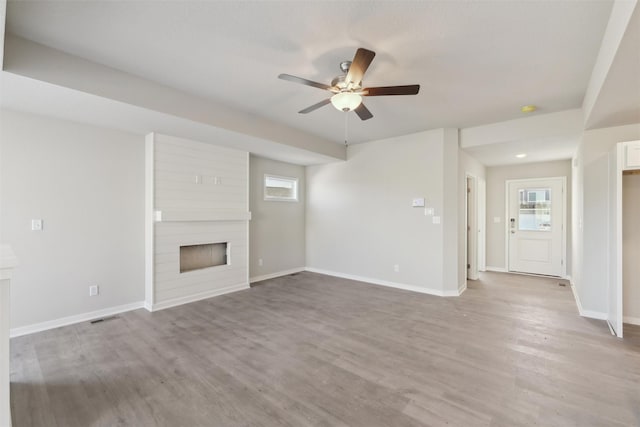 unfurnished living room featuring hardwood / wood-style flooring, a large fireplace, and ceiling fan