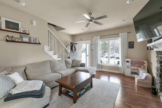 living room featuring a textured ceiling, ceiling fan, a fireplace, and wood-type flooring