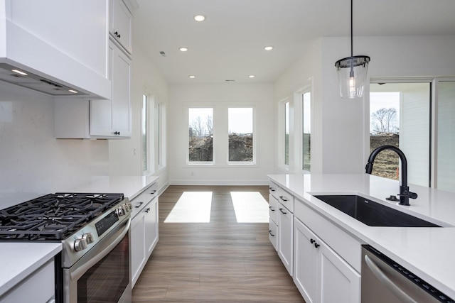 kitchen featuring pendant lighting, sink, wall chimney range hood, appliances with stainless steel finishes, and white cabinets