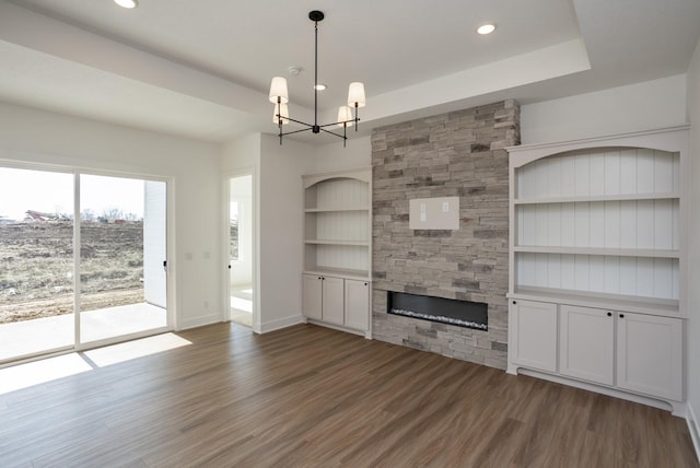 unfurnished living room featuring dark hardwood / wood-style flooring, a raised ceiling, built in features, a notable chandelier, and a fireplace