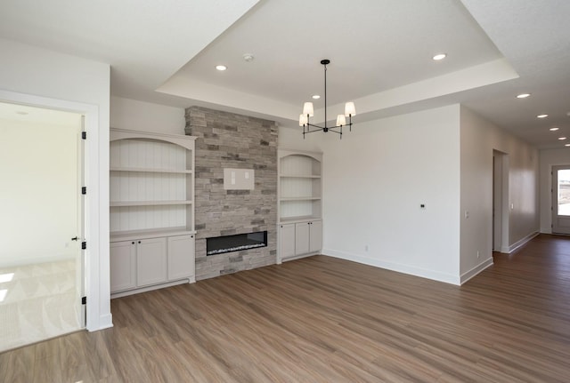 unfurnished living room with built in shelves, hardwood / wood-style floors, a fireplace, and a tray ceiling