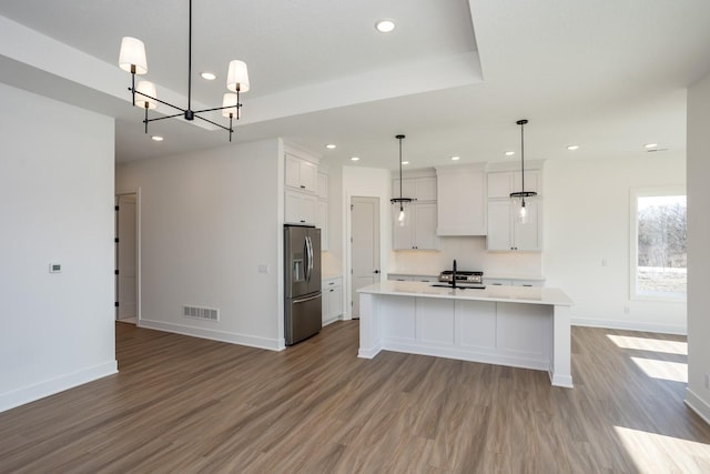 kitchen featuring an island with sink, white cabinetry, hanging light fixtures, stainless steel refrigerator with ice dispenser, and light hardwood / wood-style flooring