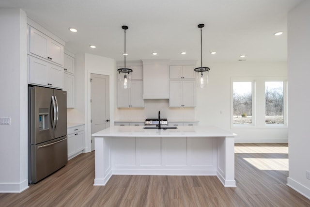 kitchen with an island with sink, wall chimney exhaust hood, stainless steel fridge with ice dispenser, and white cabinets