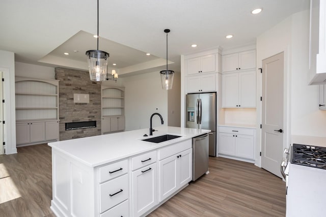 kitchen with sink, white cabinetry, stainless steel appliances, a center island with sink, and decorative light fixtures