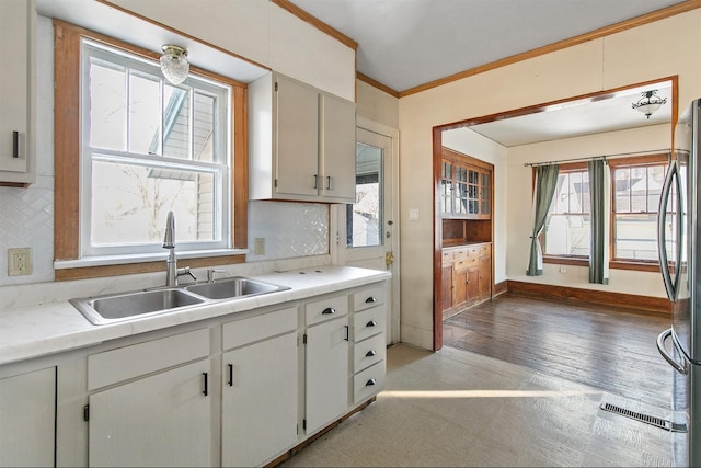 kitchen with backsplash, stainless steel refrigerator, ornamental molding, white cabinets, and sink