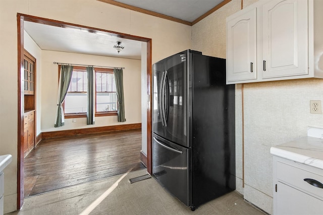 kitchen with white cabinets, dark wood-type flooring, ornamental molding, and black fridge