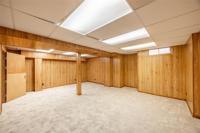 basement featuring carpet, a paneled ceiling, and wooden walls