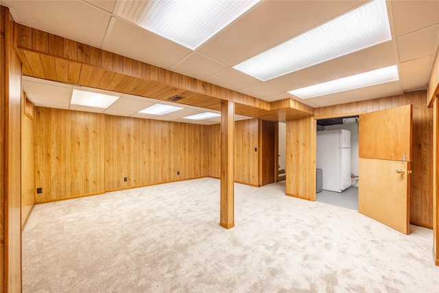 basement with carpet floors, a drop ceiling, wooden walls, and white refrigerator