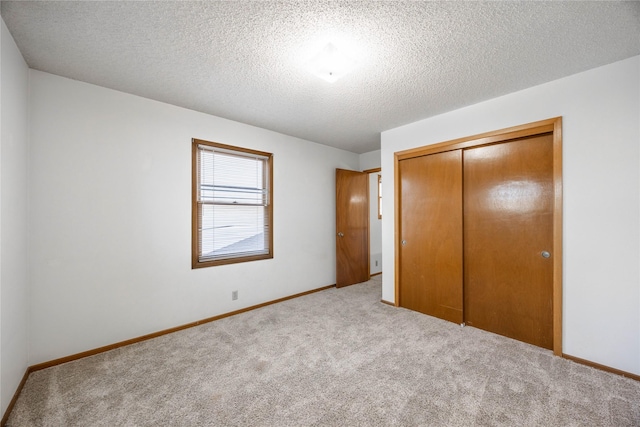 unfurnished bedroom featuring a textured ceiling, a closet, and light colored carpet