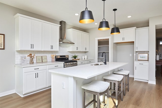 kitchen with wall chimney range hood, sink, stainless steel range with gas stovetop, and white cabinetry