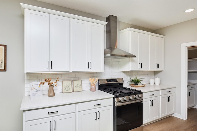 kitchen featuring stainless steel range with gas cooktop, decorative backsplash, white cabinets, wall chimney range hood, and light hardwood / wood-style flooring