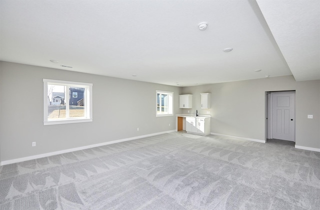 unfurnished living room with light carpet, plenty of natural light, and sink