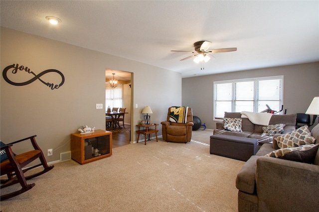 carpeted living room with ceiling fan with notable chandelier