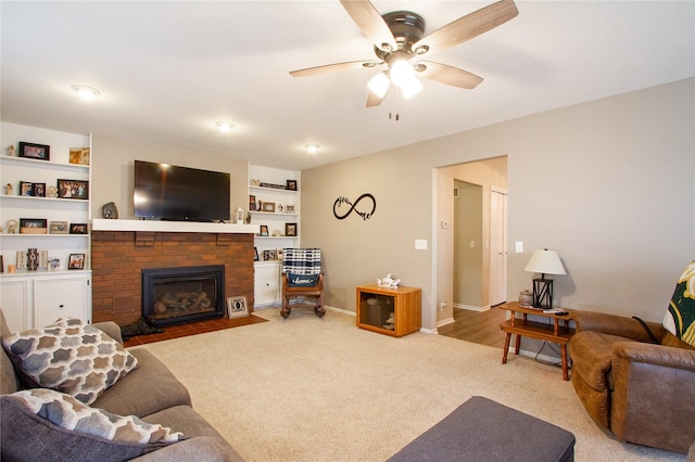 living room featuring a brick fireplace, built in shelves, light colored carpet, and ceiling fan