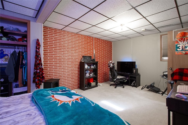 bedroom featuring carpet floors, a closet, a drop ceiling, and brick wall