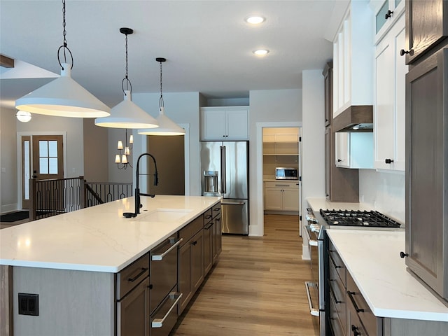 kitchen featuring a kitchen island with sink, light wood-style flooring, a sink, appliances with stainless steel finishes, and pendant lighting