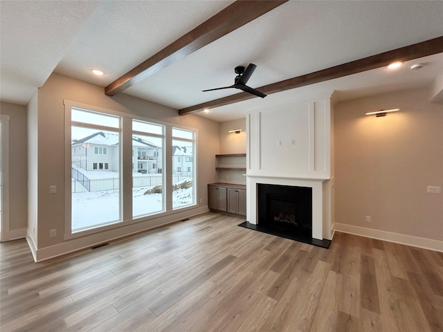 unfurnished living room with a fireplace, light wood finished floors, a textured ceiling, beamed ceiling, and baseboards