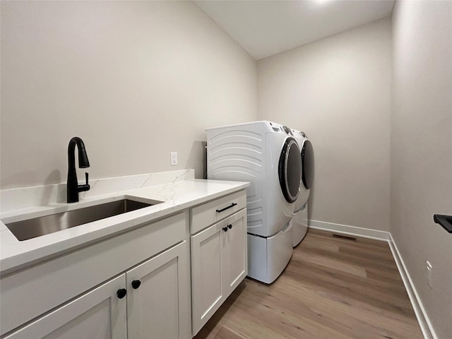 clothes washing area featuring a sink, baseboards, light wood-style floors, washer and dryer, and cabinet space