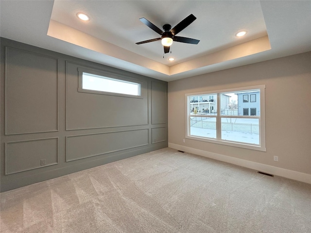 spare room featuring a tray ceiling, light colored carpet, and a decorative wall