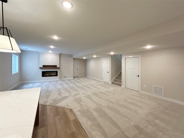 unfurnished living room featuring baseboards, visible vents, a glass covered fireplace, stairway, and recessed lighting