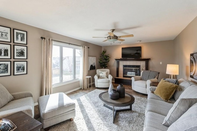 living room with ceiling fan, a tiled fireplace, and hardwood / wood-style flooring