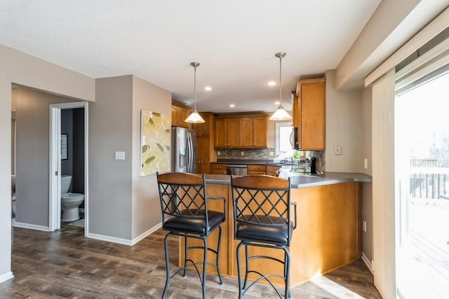 kitchen featuring a kitchen bar, kitchen peninsula, appliances with stainless steel finishes, decorative backsplash, and hanging light fixtures