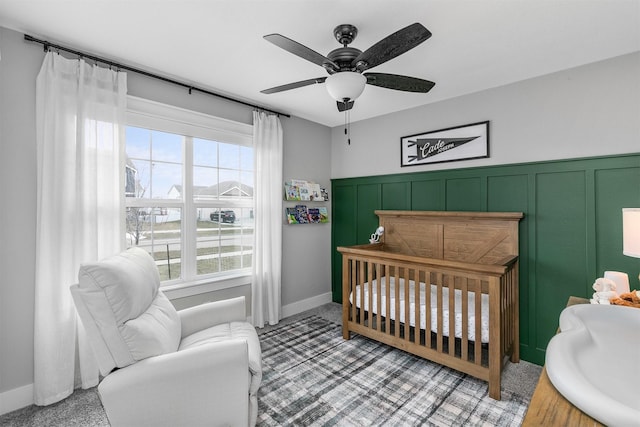 carpeted bedroom with ceiling fan and a nursery area