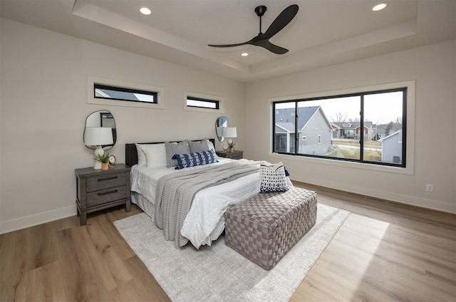 bedroom featuring baseboards, recessed lighting, light wood-style flooring, and a tray ceiling