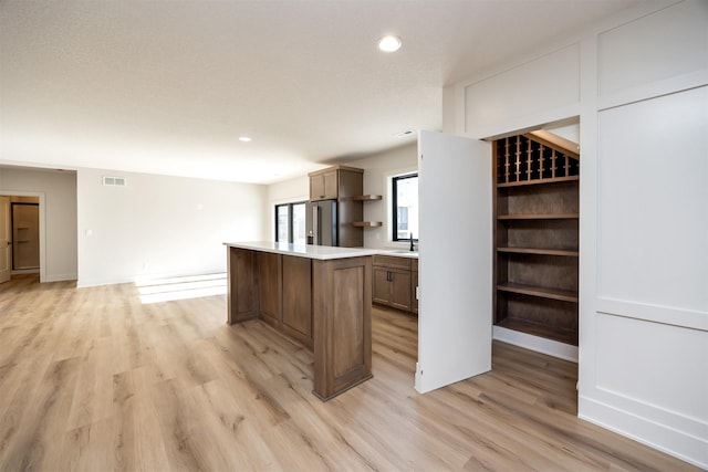 kitchen with open shelves, light wood-style floors, high end refrigerator, a kitchen island, and visible vents
