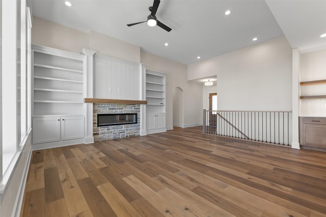 unfurnished living room with built in features, a stone fireplace, and hardwood / wood-style floors