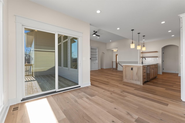 kitchen with decorative light fixtures, light hardwood / wood-style floors, a kitchen island with sink, ceiling fan, and stainless steel dishwasher