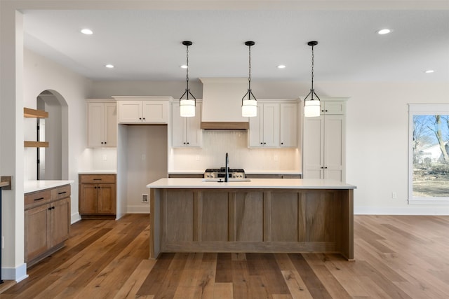 kitchen with light hardwood / wood-style floors, a center island with sink, and tasteful backsplash