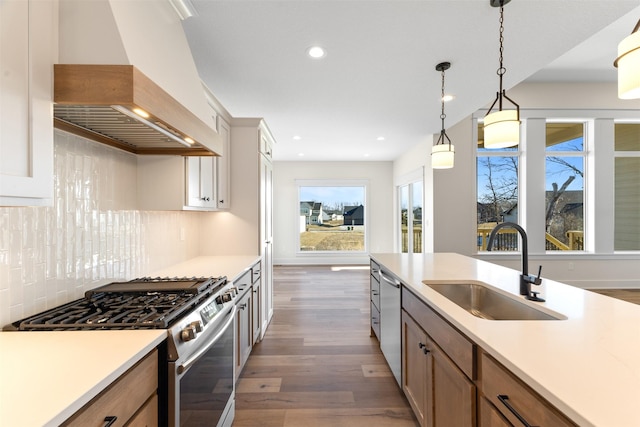 kitchen featuring pendant lighting, appliances with stainless steel finishes, tasteful backsplash, sink, and custom range hood