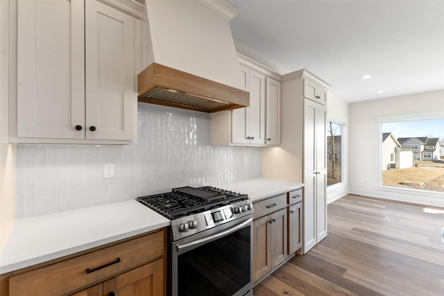 kitchen with white cabinetry, decorative backsplash, light wood-type flooring, stainless steel range with gas cooktop, and custom range hood