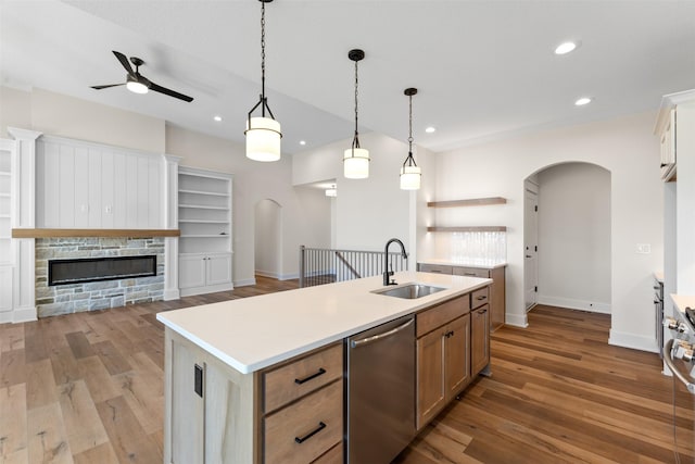 kitchen with a center island with sink, decorative light fixtures, a fireplace, dishwasher, and sink