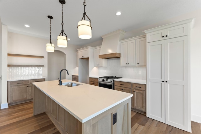 kitchen with stainless steel range with gas cooktop, a center island with sink, sink, and custom range hood