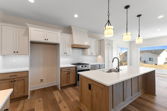 kitchen featuring premium range hood, white cabinetry, stainless steel gas range, a kitchen island with sink, and sink