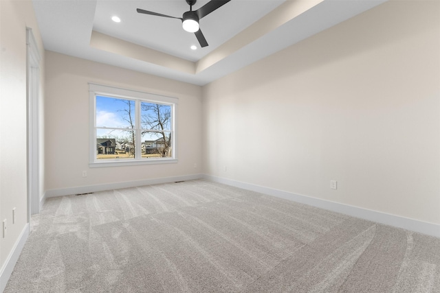 empty room with ceiling fan, light colored carpet, and a tray ceiling