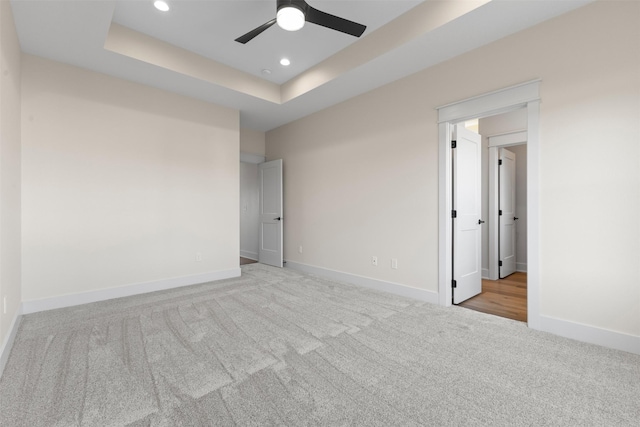 spare room with ceiling fan, light colored carpet, and a raised ceiling