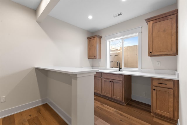 kitchen with wood-type flooring, kitchen peninsula, and sink