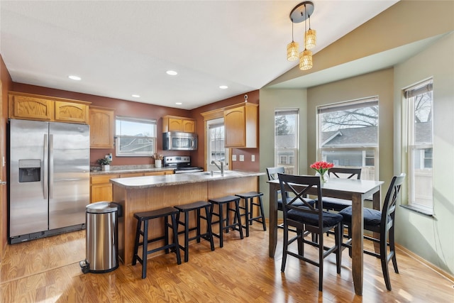 kitchen with lofted ceiling, kitchen peninsula, light hardwood / wood-style flooring, hanging light fixtures, and stainless steel appliances