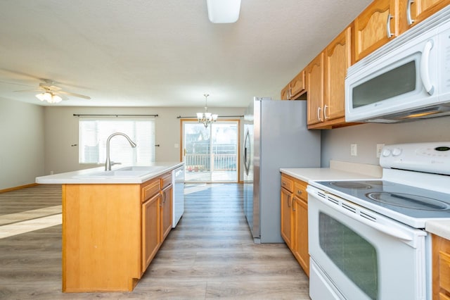 kitchen featuring decorative light fixtures, a center island with sink, sink, white appliances, and light hardwood / wood-style flooring