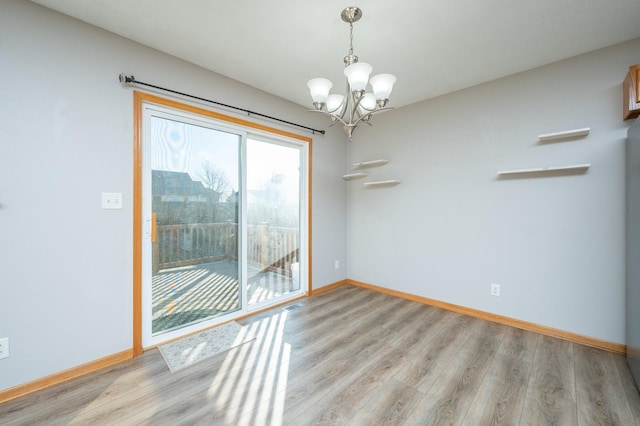 spare room featuring an inviting chandelier, baseboards, light wood finished floors, and visible vents