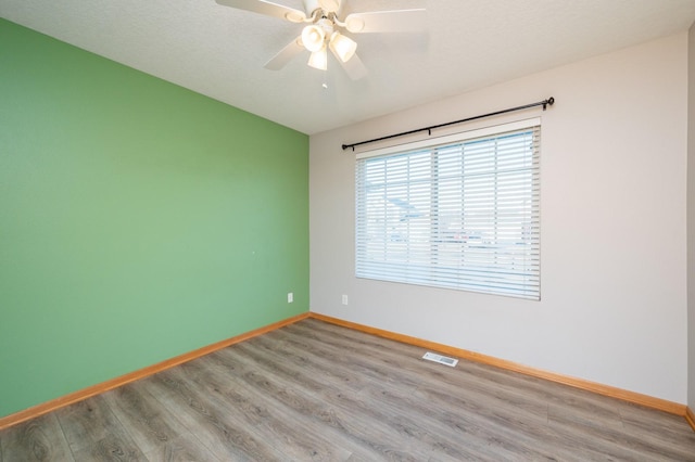 empty room featuring baseboards, a ceiling fan, wood finished floors, and visible vents