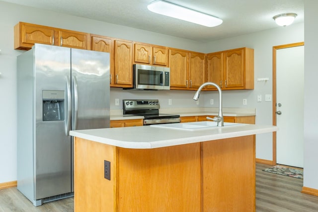 kitchen featuring an island with sink, light wood-type flooring, light countertops, a sink, and stainless steel appliances