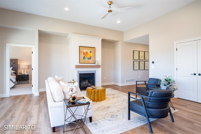 living room with light wood-type flooring, ceiling fan, and a fireplace