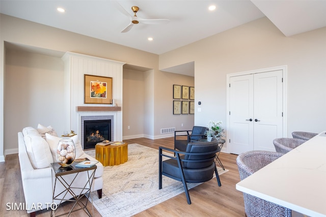 living room featuring ceiling fan, light wood-type flooring, and a fireplace