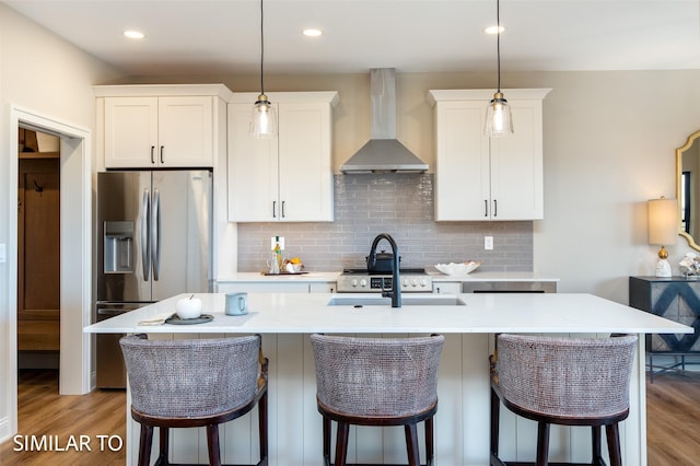 kitchen with stainless steel refrigerator with ice dispenser, white cabinets, wall chimney exhaust hood, and a kitchen island with sink